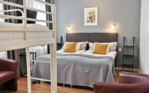 Un dormitorio con una cama litera, una cama individual con una colcha gris y almohadas amarillas, un cuadro en la pared y una mesita.