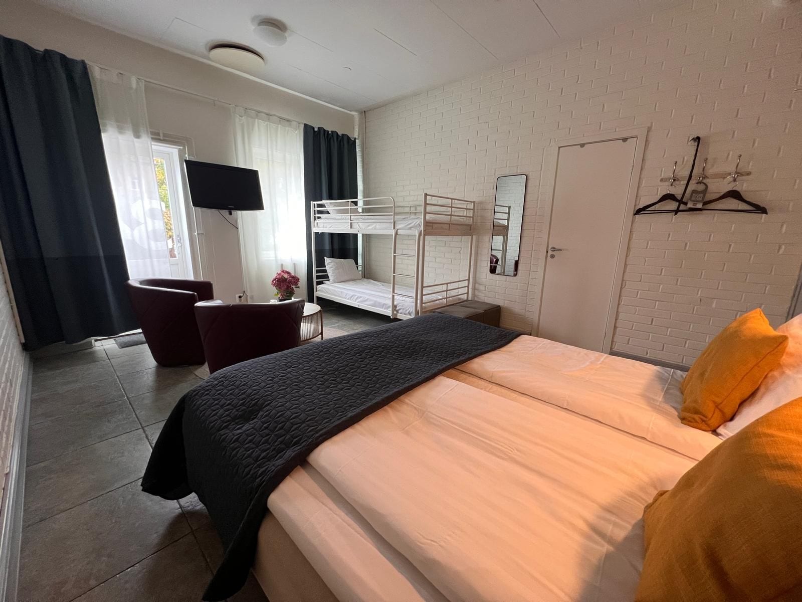 Una habitación de hotel con literas, un escritorio con silla, un espejo y un armario.