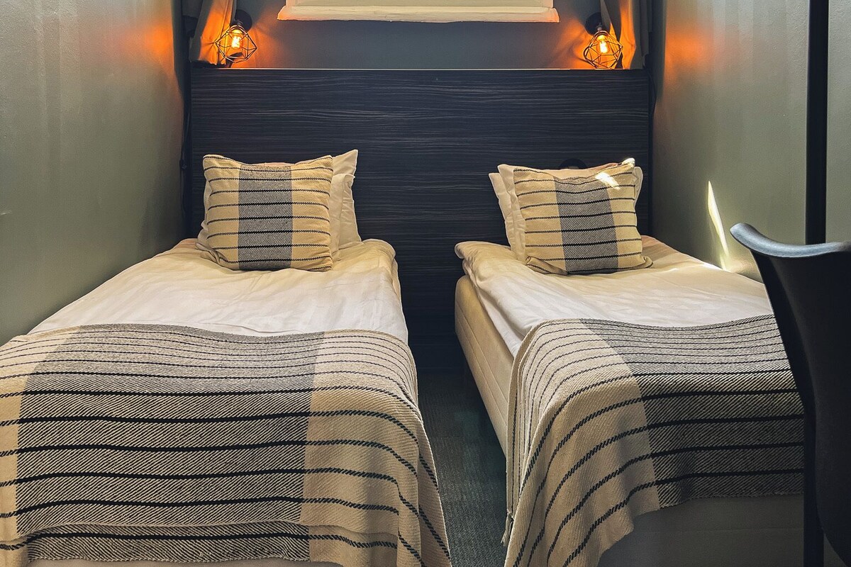 Una habitación con dos camas, una ventana con cortinas y una lámpara fijada a la pared.