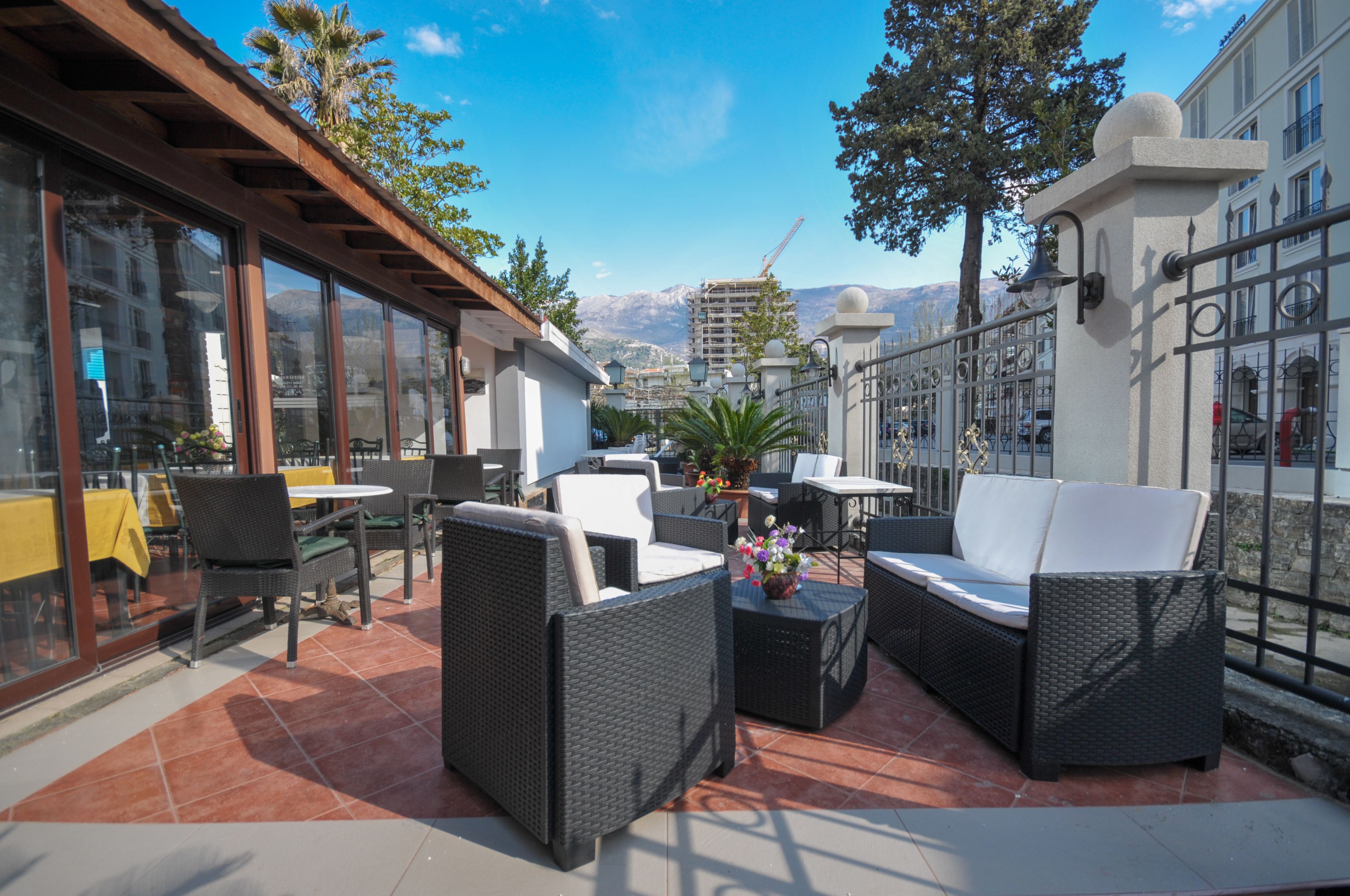 An outdoor patio with wicker furniture, a table with a yellow tablecloth, and a view of mountains in the background.