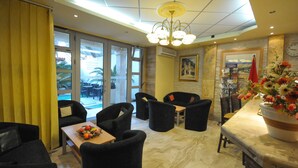 A hotel lobby with a dining area, black upholstered chairs, a marble floor, and a large window with a view of the outdoors. - Oaza (Budva)