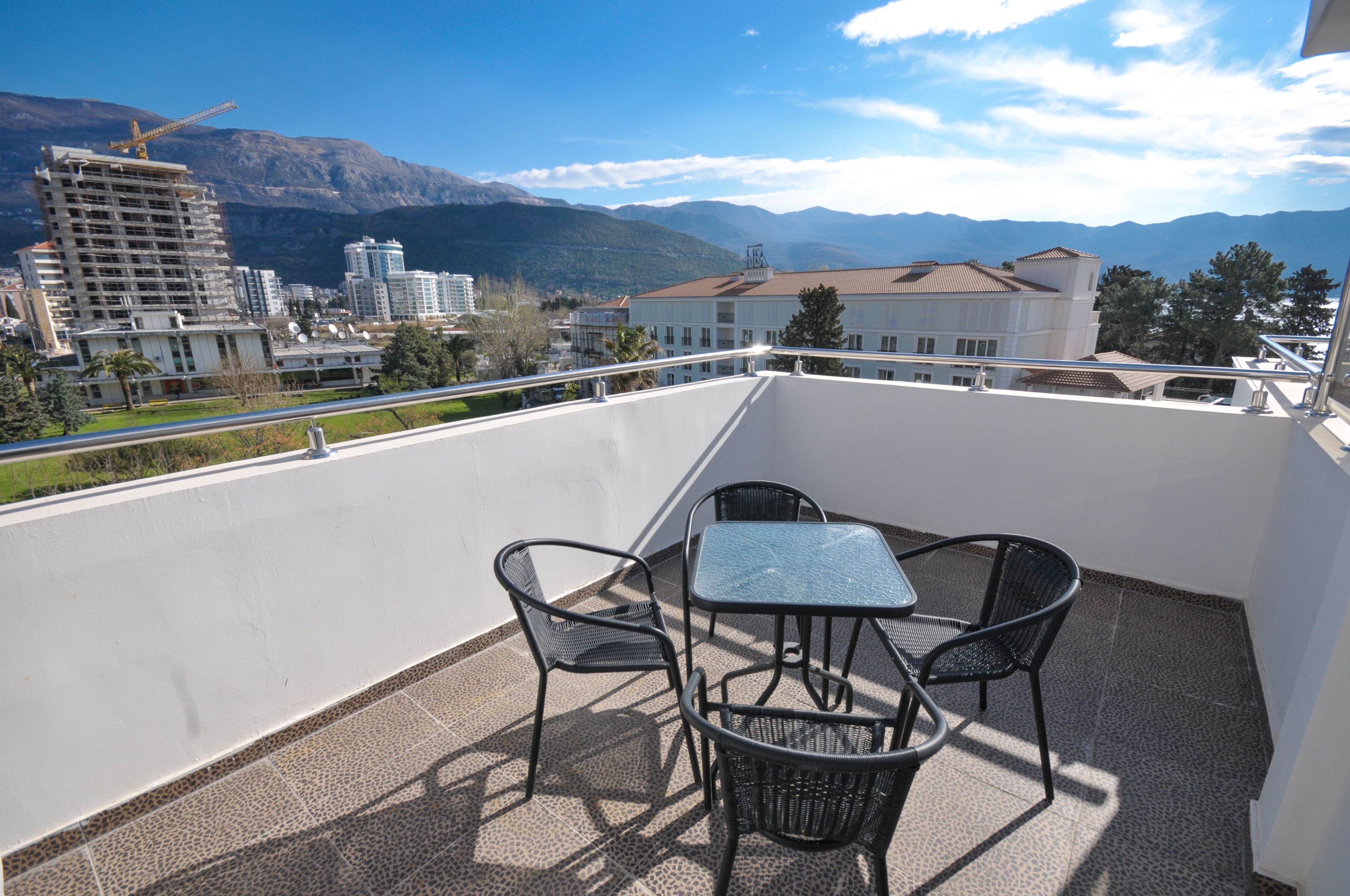 Un balcone con tavolo e sedie, affacciato su una città con montagne sullo sfondo.