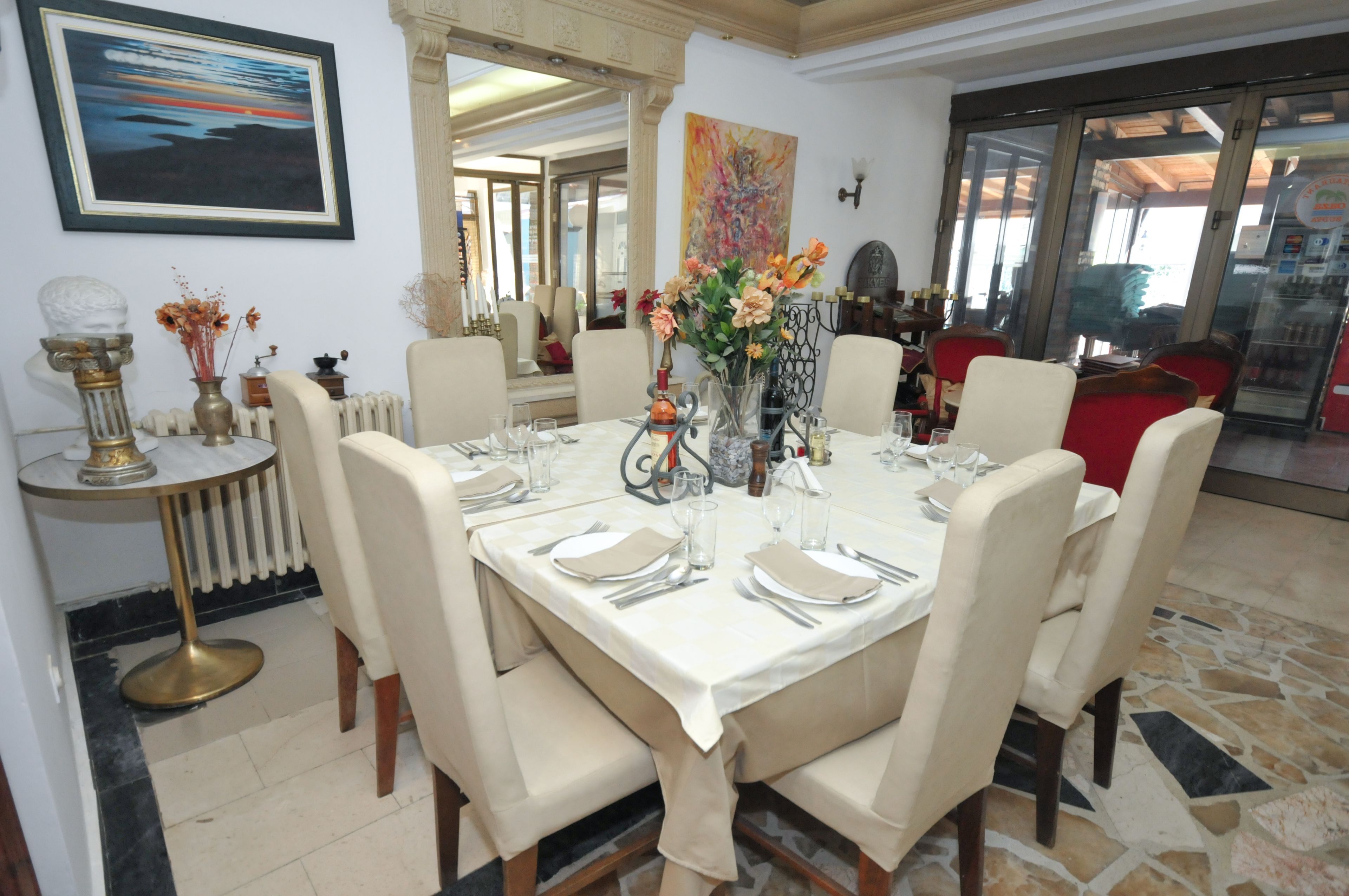 A dining area with a large table set for six, surrounded by chairs. There is a vase with flowers on the table, and a radiator is visible to the left.