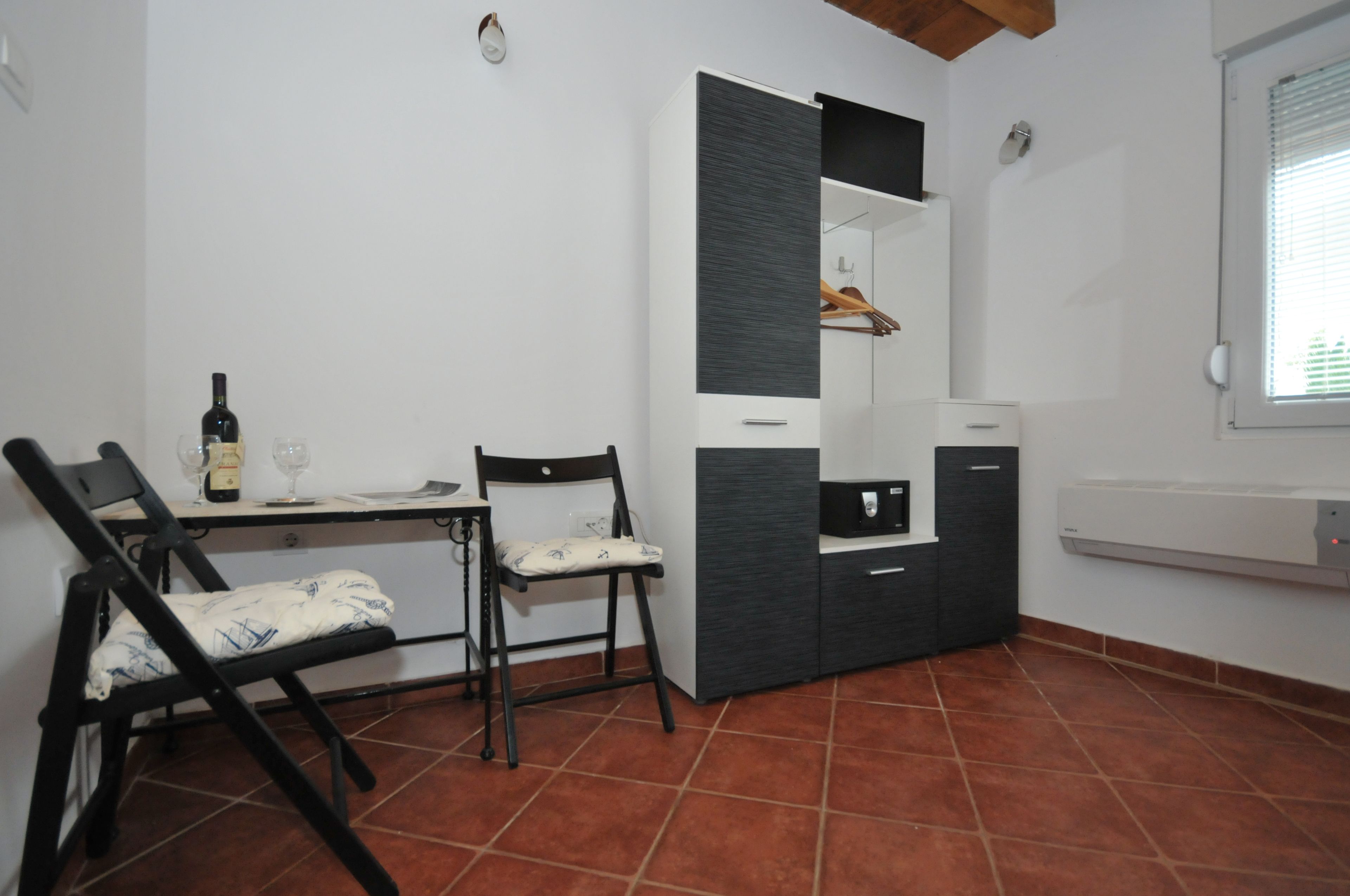 A compact room with a dining table, two chairs, a minibar, and a window with blinds.