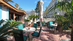 An outdoor patio area with round tables and chairs, surrounded by potted plants and umbrellas. - Oaza (Budva)