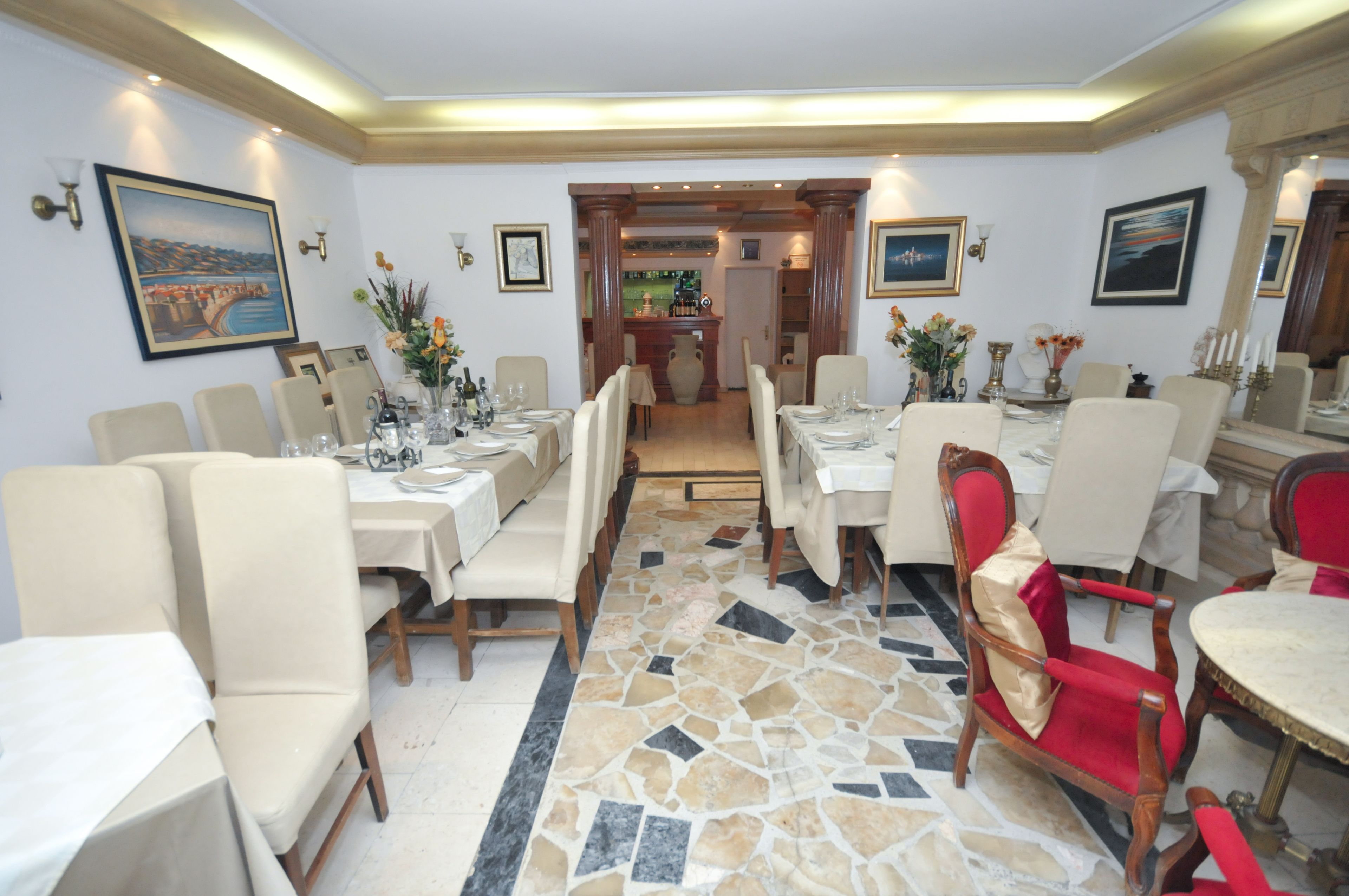 A dining area with multiple tables and chairs, a tiled floor, and framed artwork on the walls.