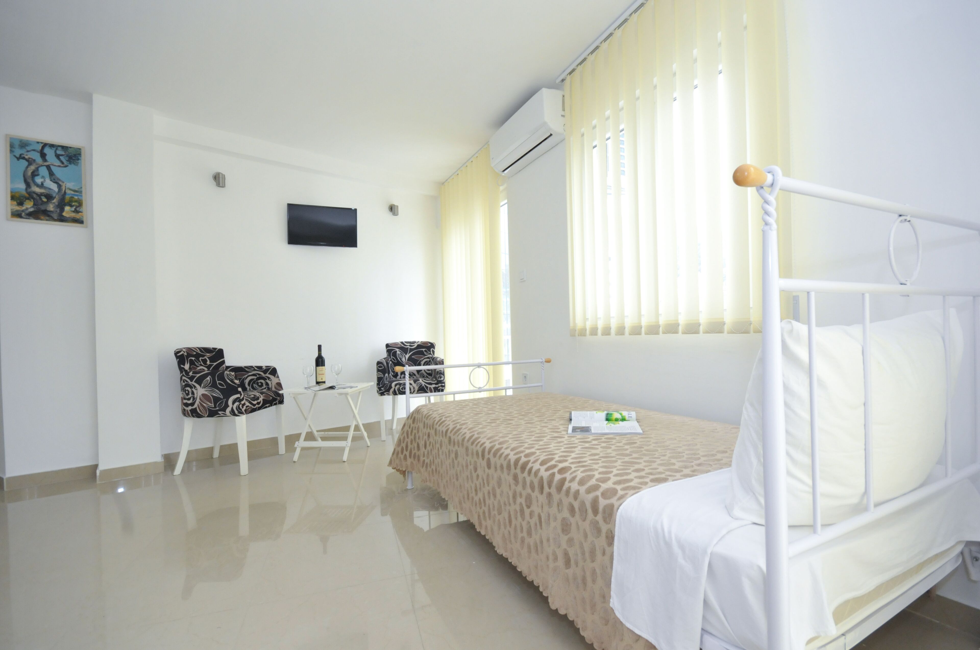 Una habitación de hotel con cama, televisión, una mesita con sillas y ventana con cortinas.
