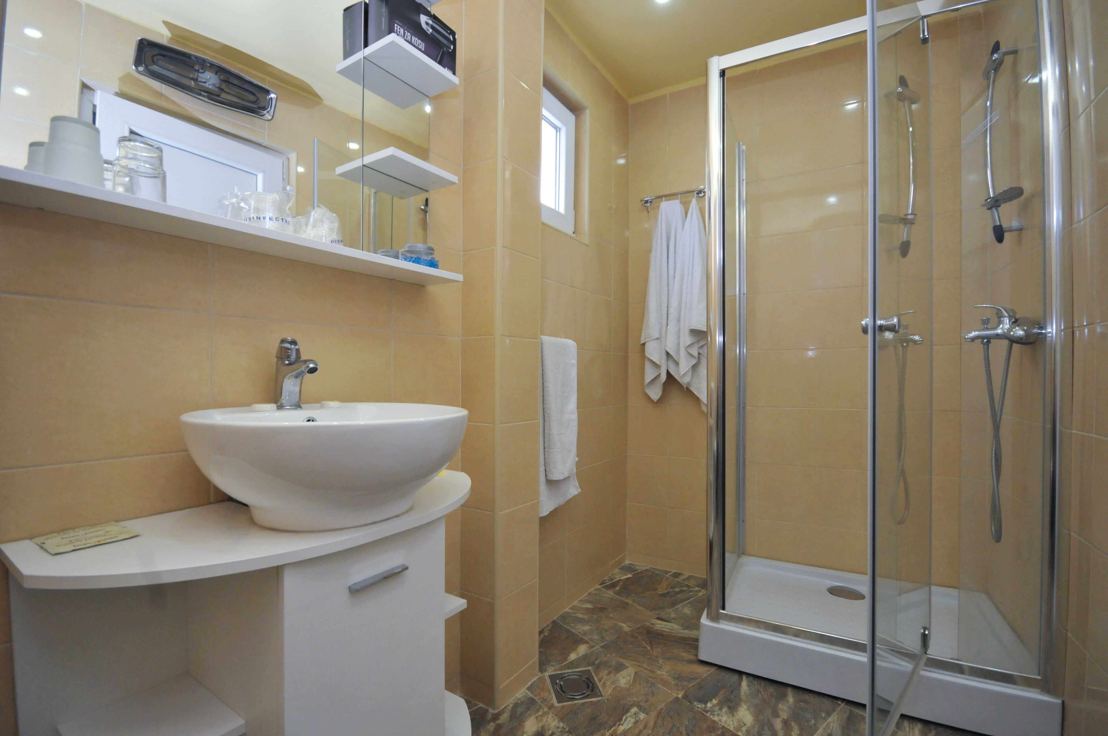 A modern bathroom with a large white sink, a glass-enclosed shower, and beige tiled walls.