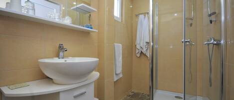 A modern bathroom with a large white sink, a glass-enclosed shower, and beige tiled walls.