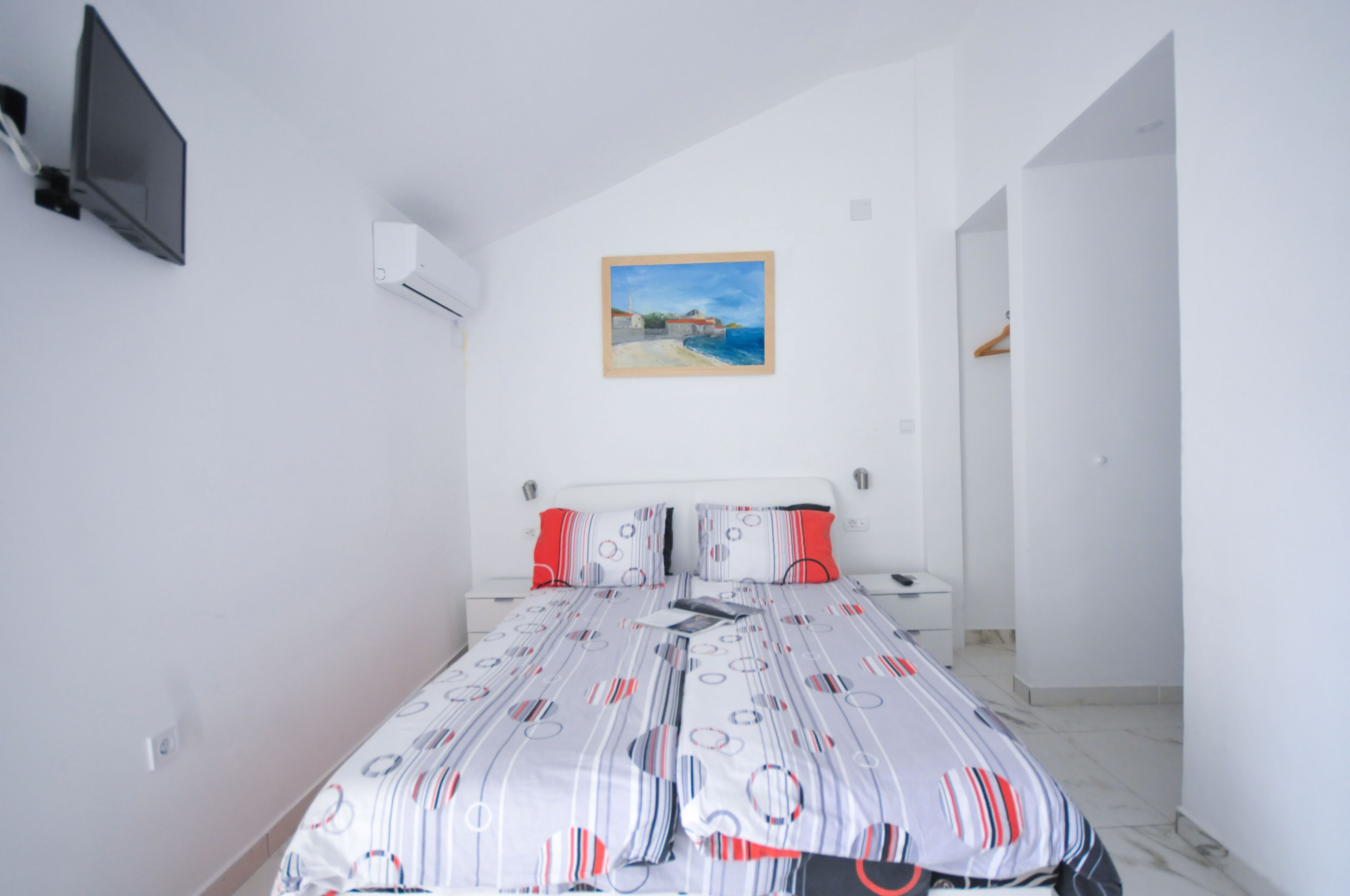 Un dormitorio con una cama, un cuadro en la pared y un televisor montado.
