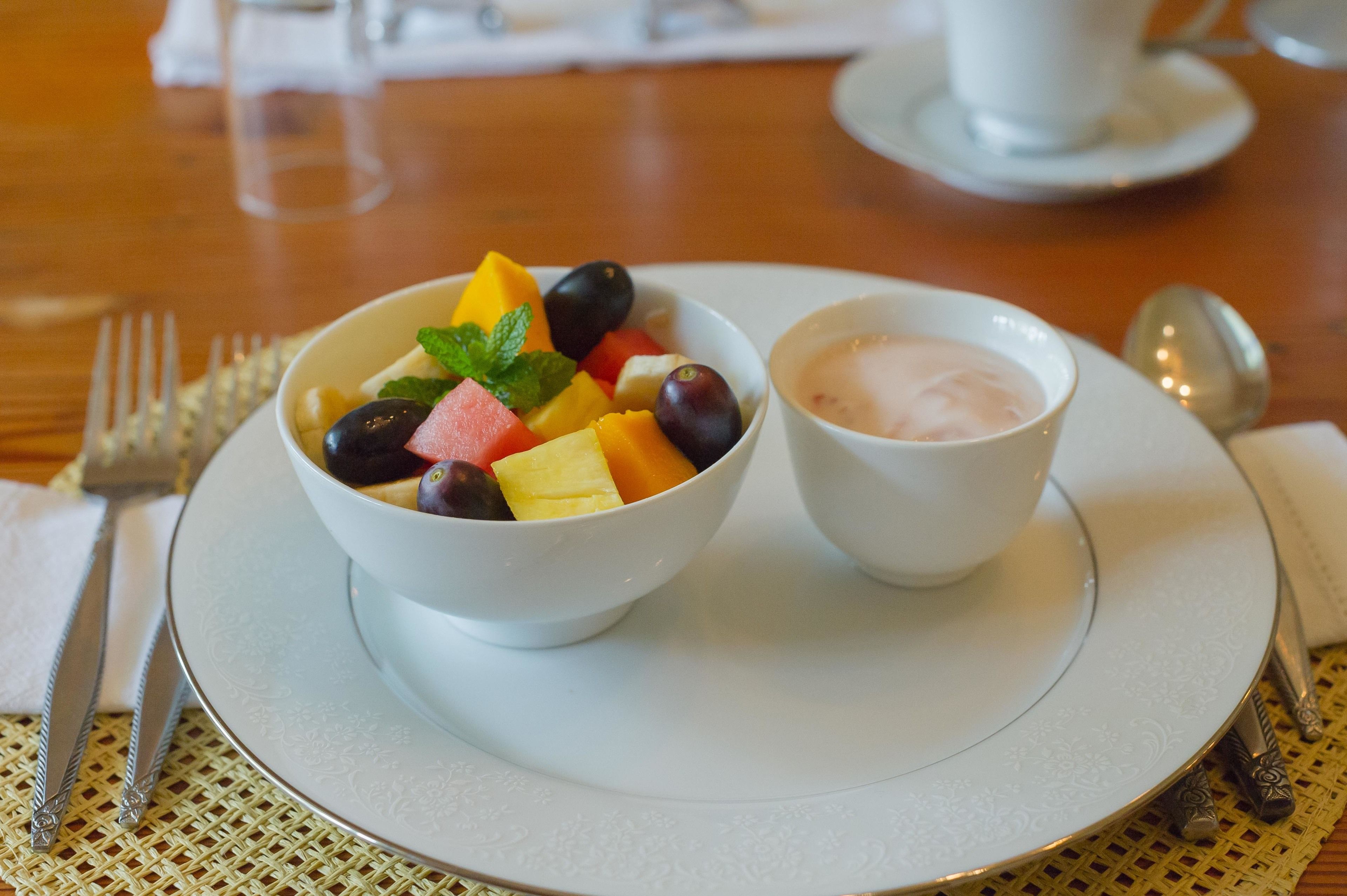 Un tazón blanco con fruta mixta y una taza pequeña blanca con una bebida rosa sobre un plato blanco.