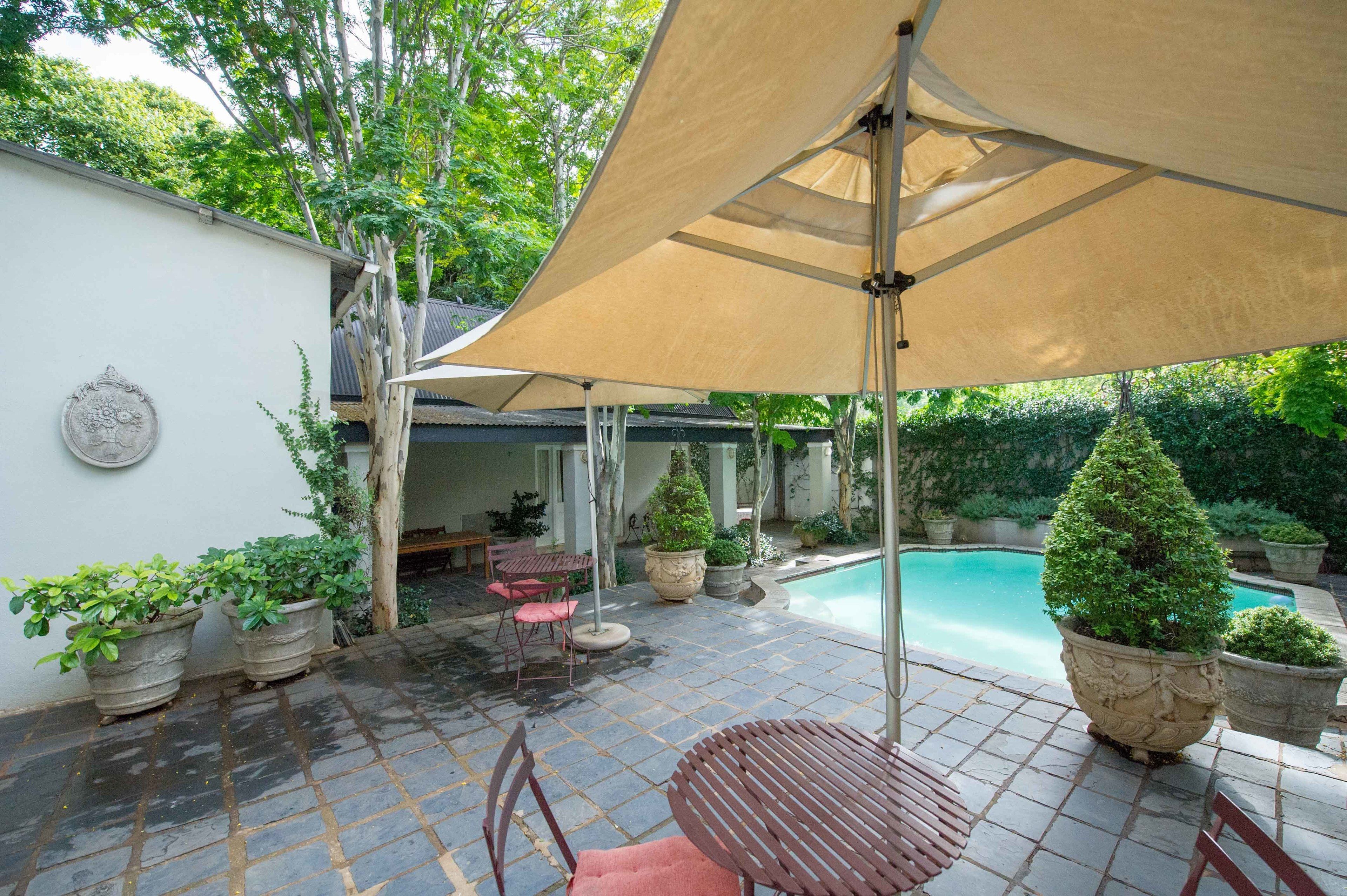 A patio area with a pool, stone tiles, potted plants, and outdoor furniture.