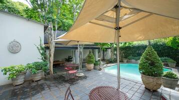 A patio area with a pool, stone tiles, potted plants, and outdoor furniture.