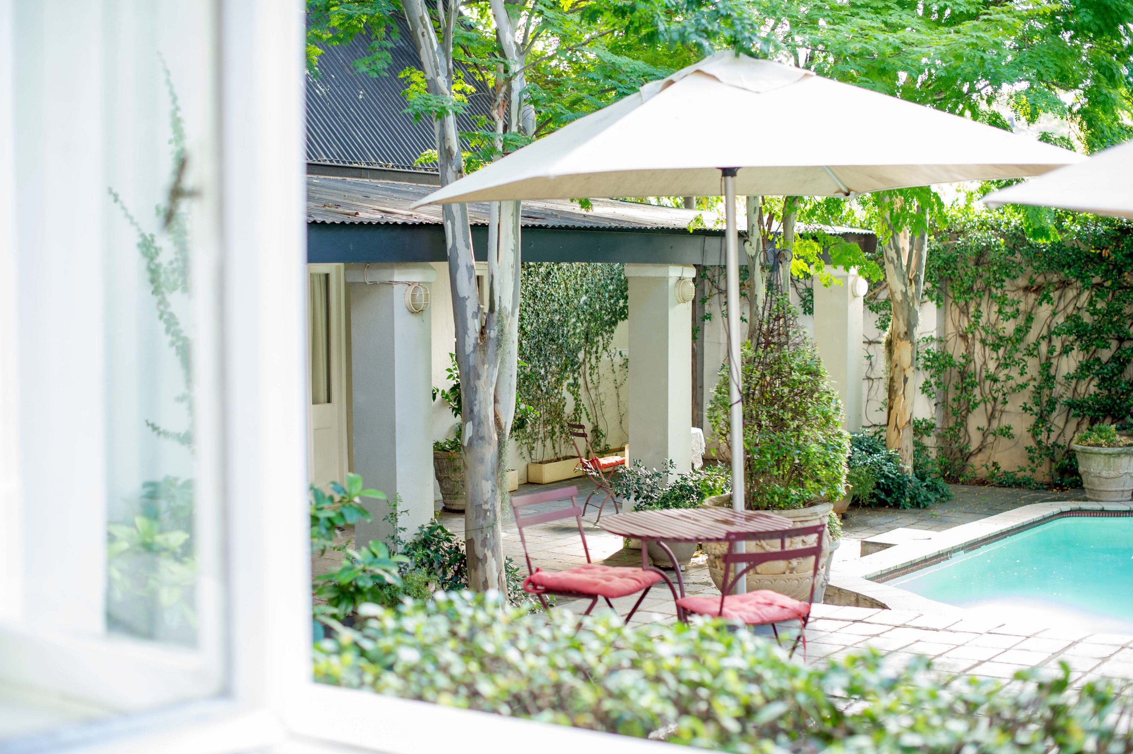 A patio area with a pool, outdoor furniture, and lush greenery.