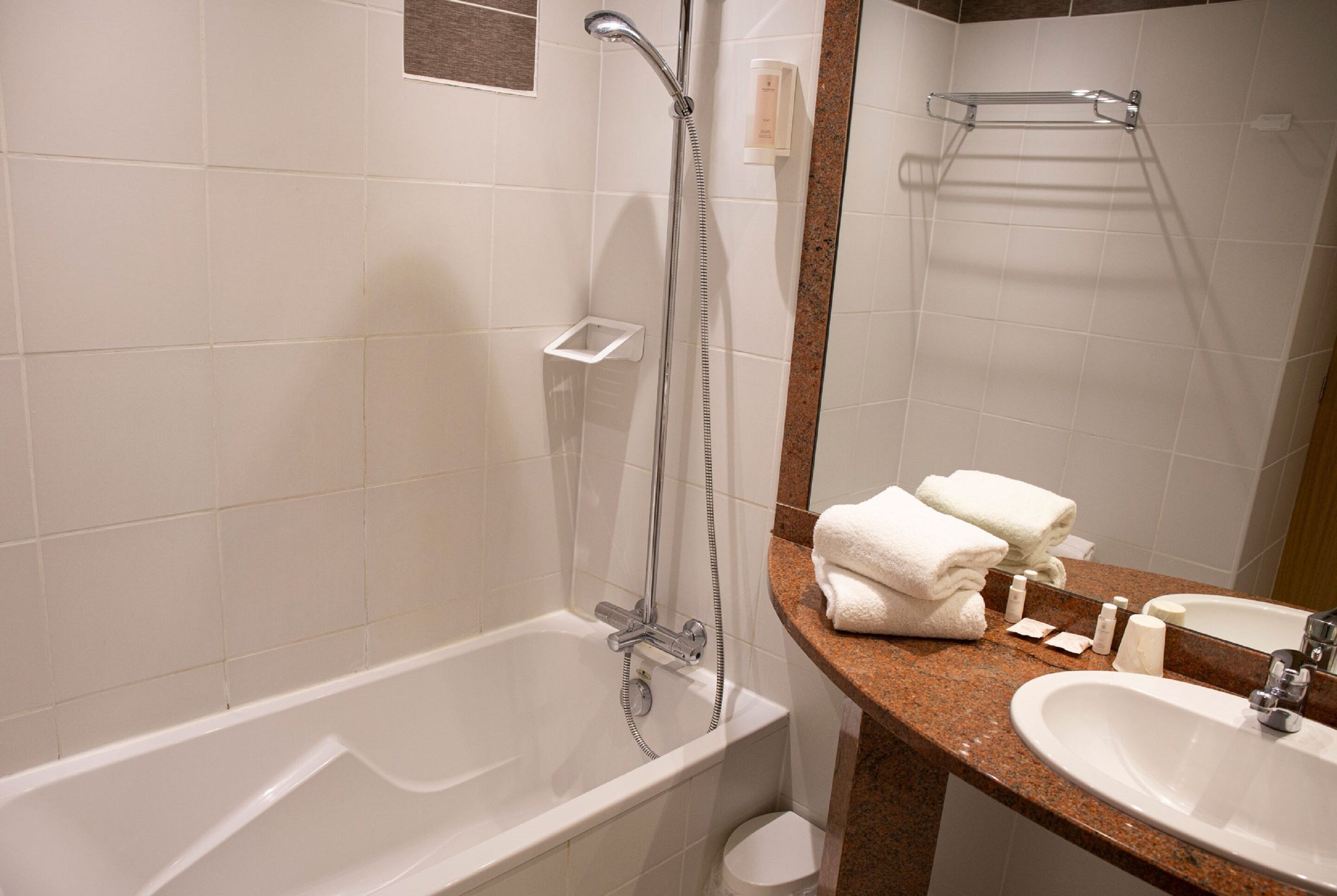 Un baño con bañera, lavamanos, espejo y toallero.