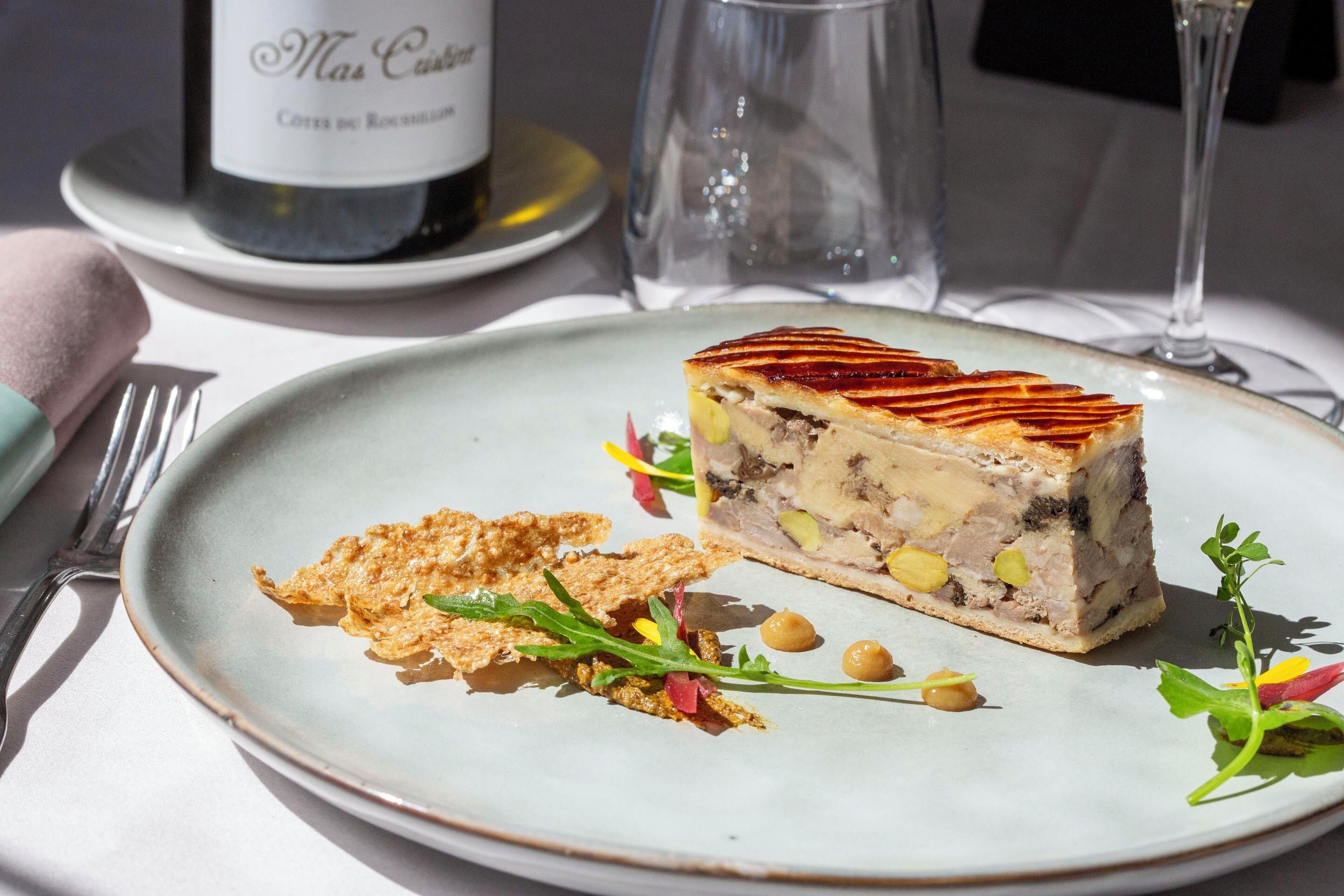 A plate with a slice of meat terrine, garnished with microgreens and chickpeas, on a light blue ceramic plate.