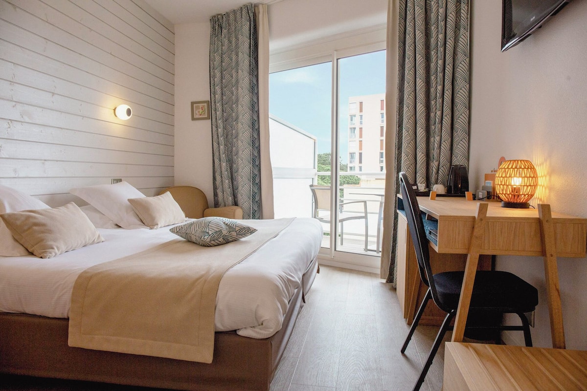 Habitación de hotel con cama, escritorio, silla, lámpara y vistas al exterior.