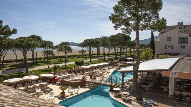 A pool area with lounge chairs and umbrellas, a pool, and a view of the beach and mountains. - Grand Hôtel du Lido (Argelès-sur-Mer)