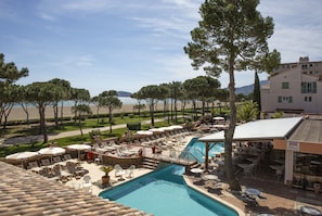 Un área de piscina con sillones de descanso y sombrillas, una piscina y vistas a la playa y las montañas.
