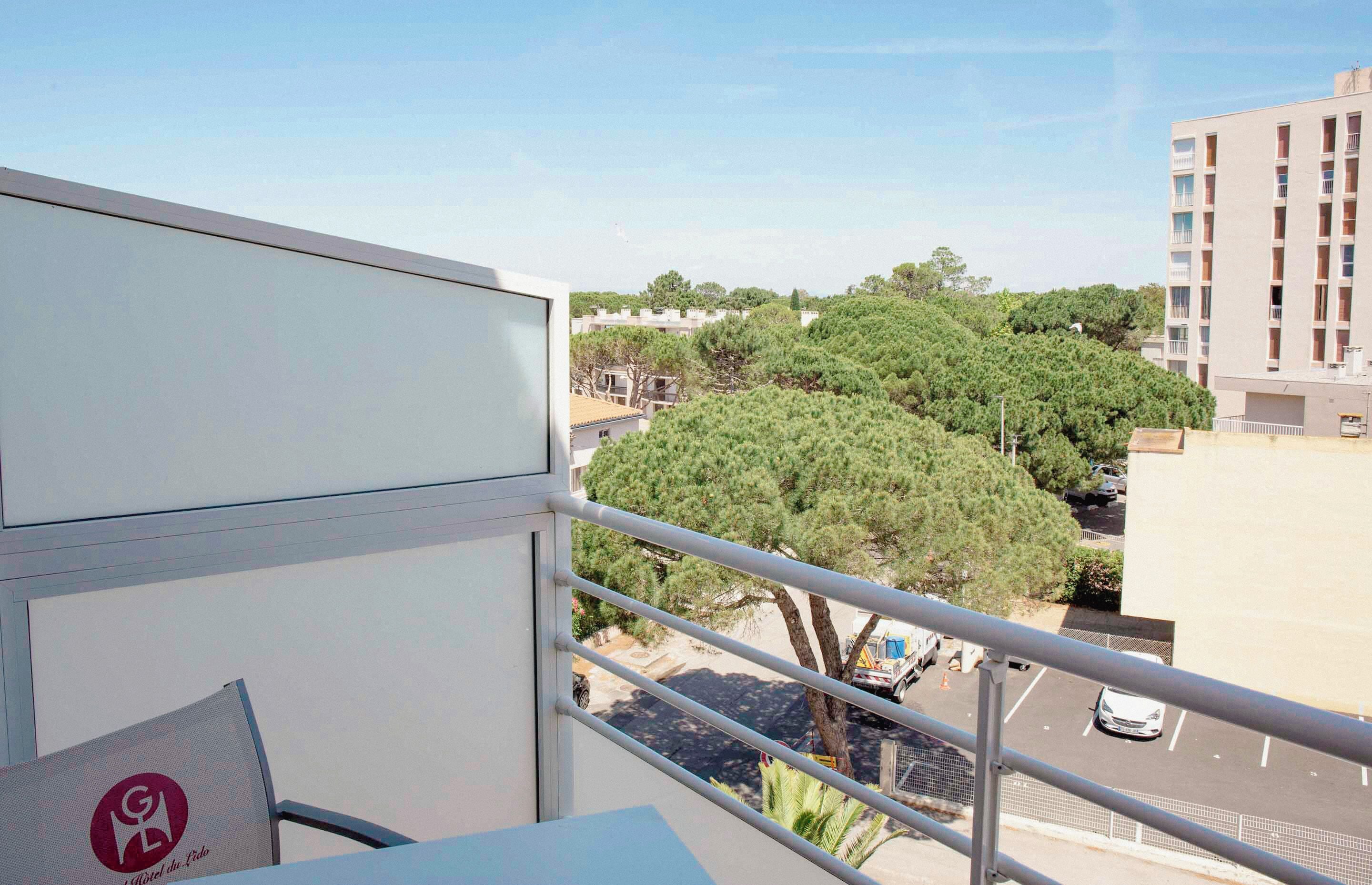 A balcony with a railing, a view of a parking lot, and a building with multiple floors in the background.
