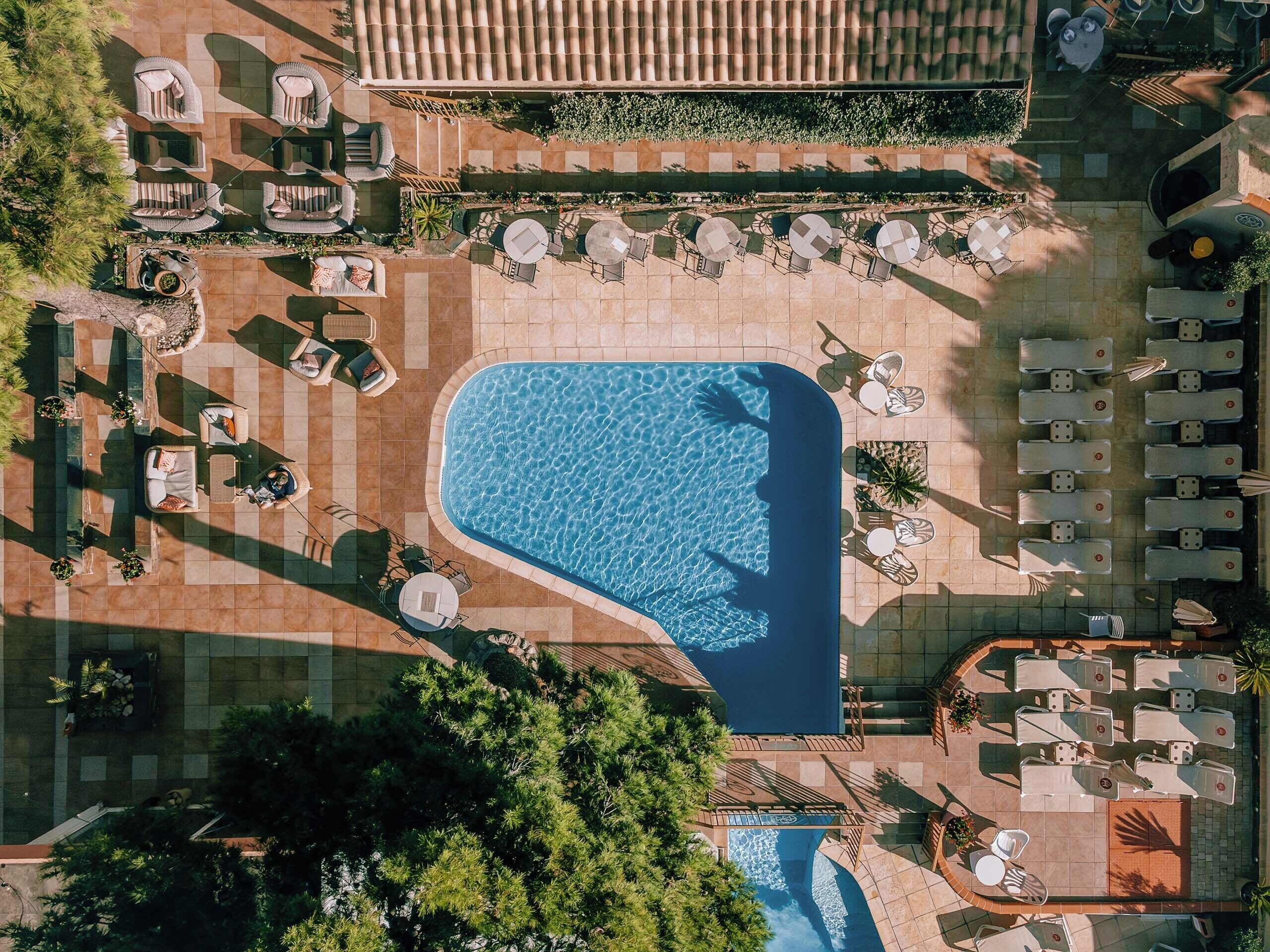 Vista aérea de un resort con piscina central, tumbonas y zonas de estar al aire libre.