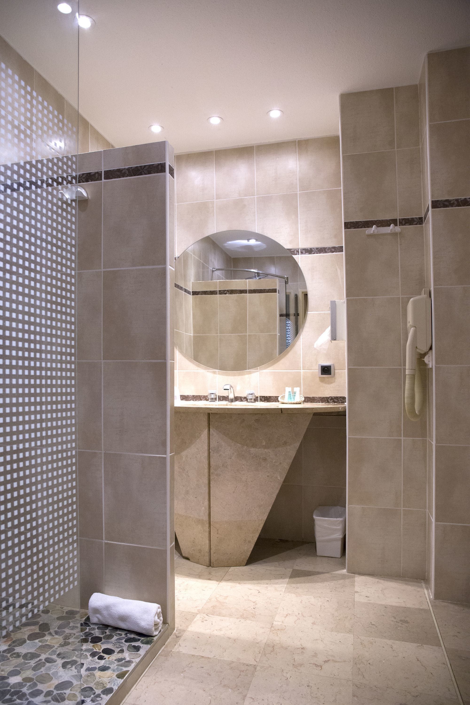 Une salle de bain moderne avec une douche à parois de verre, un miroir rond et des toilettes.