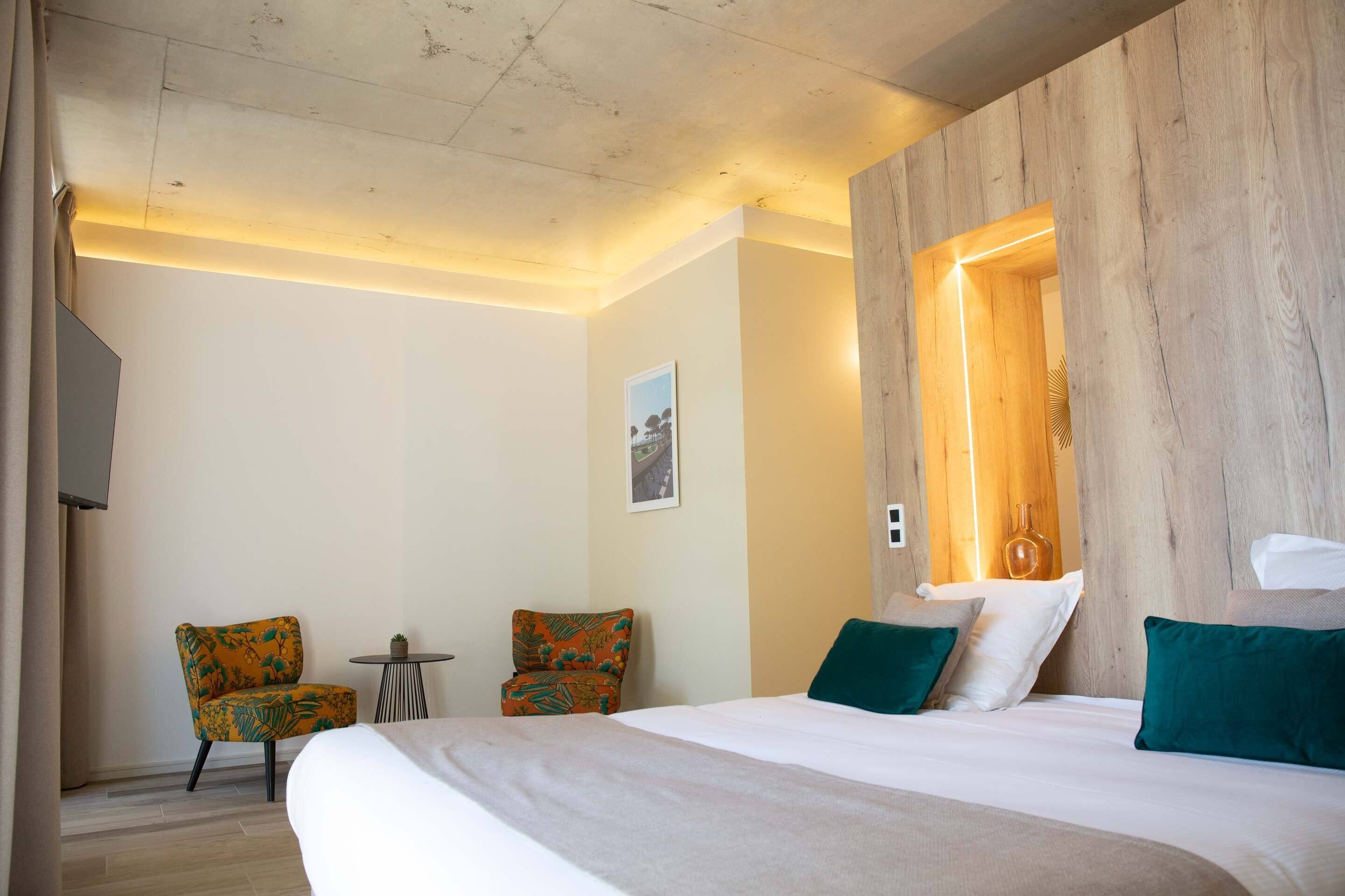 A hotel room with a large bed, two chairs, a small table, and a wooden accent wall.