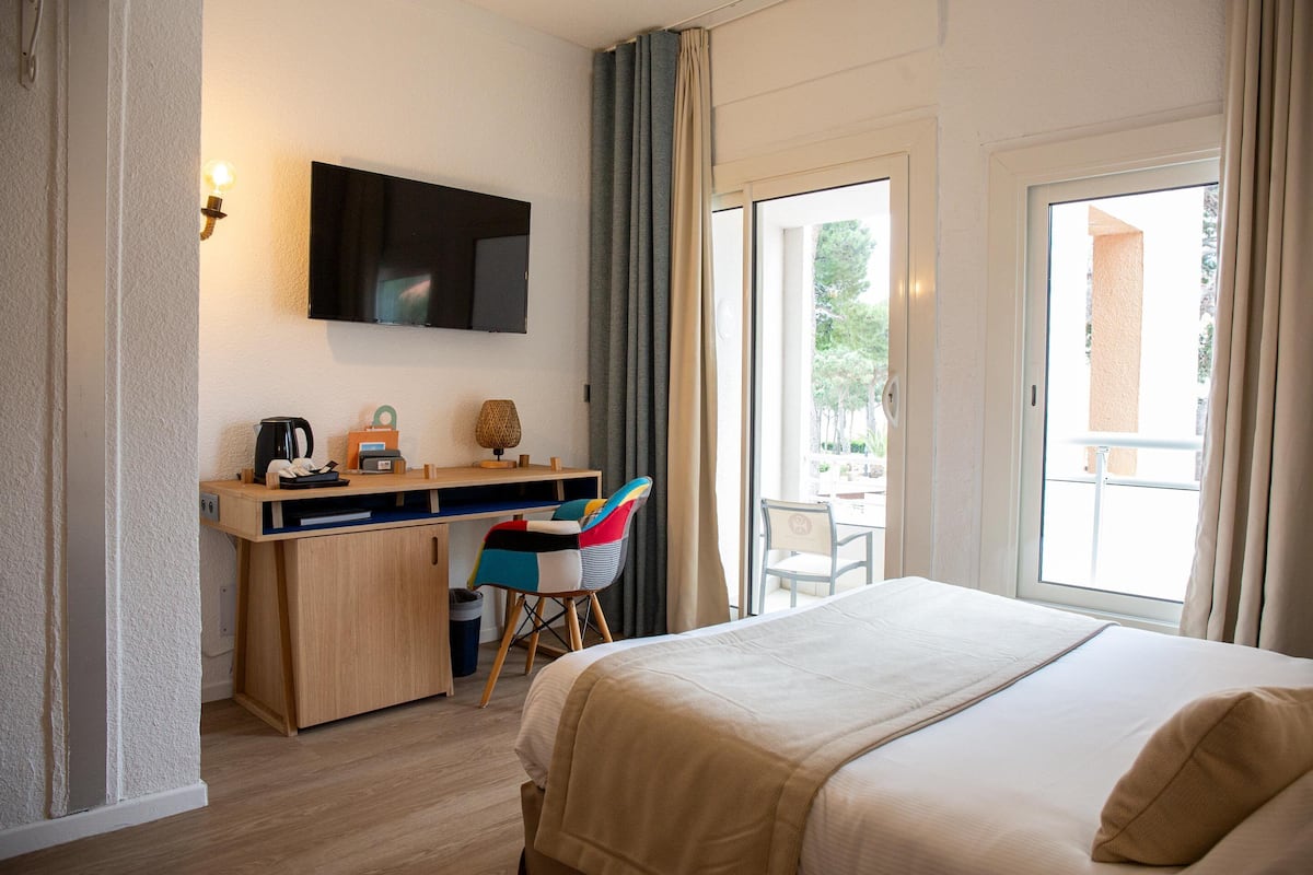 Habitación de hotel con cama, escritorio con televisor, una silla y vistas al exterior.