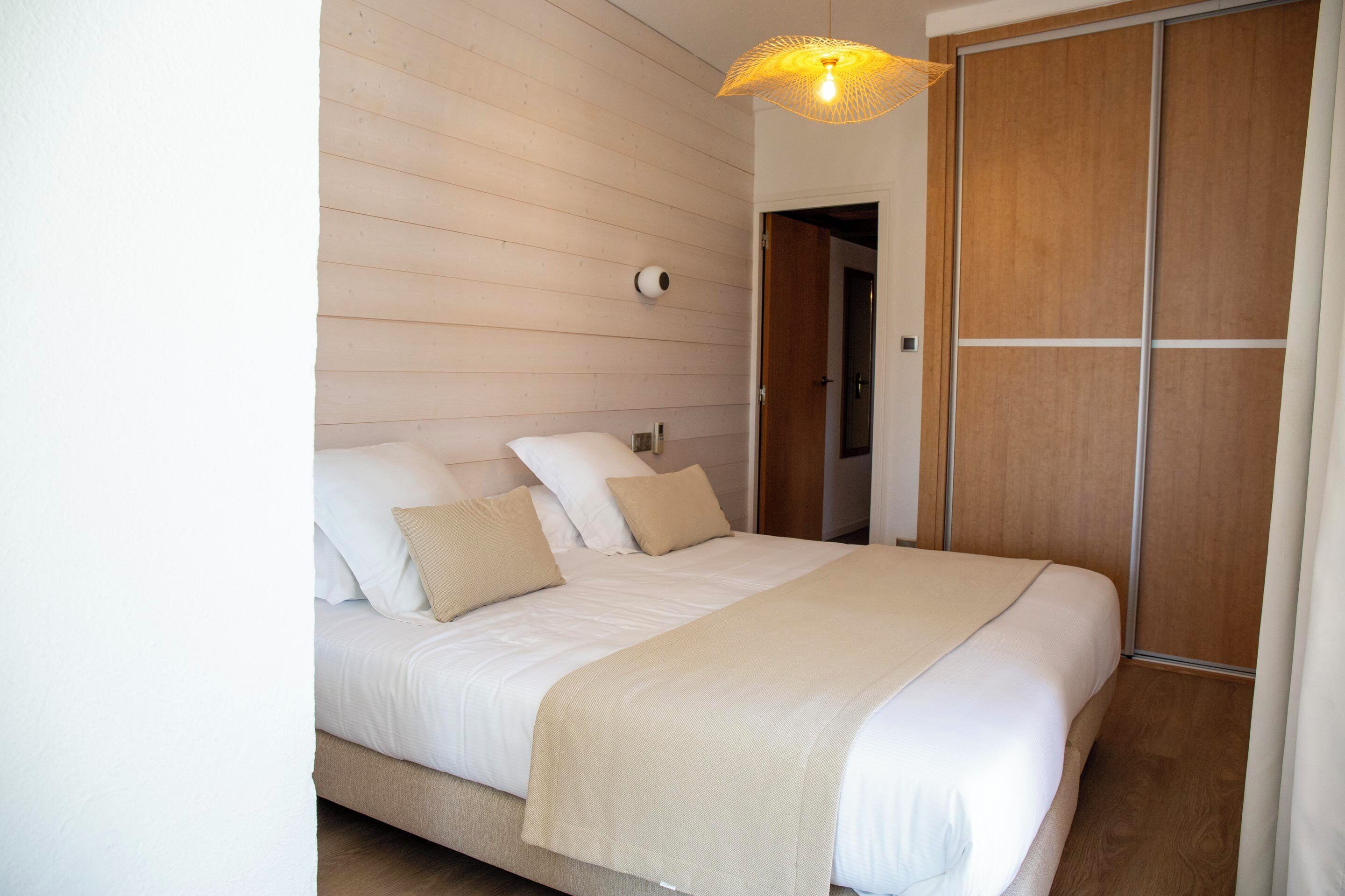 A bedroom with a bed, wooden panel walls, a wooden wardrobe, and a hanging light fixture.