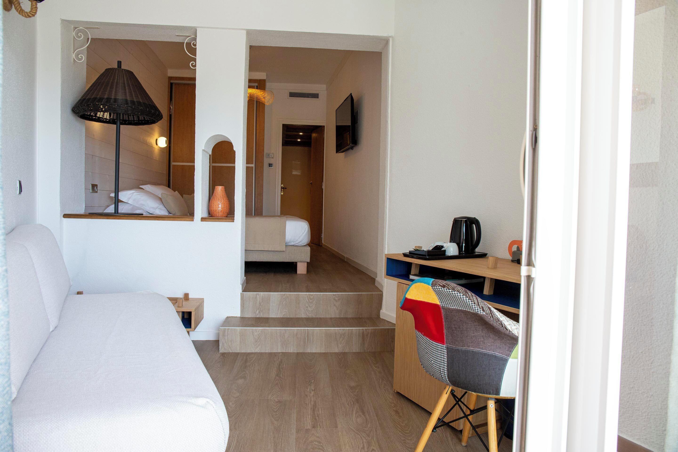 A hotel room with a bed, a desk with a chair, a lamp, and a TV on the wall.