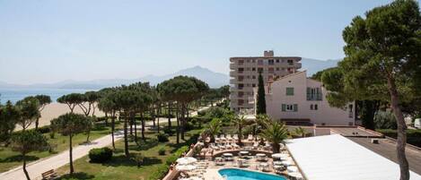 A resort with a swimming pool, lounge chairs, and a view of the beach and mountains.