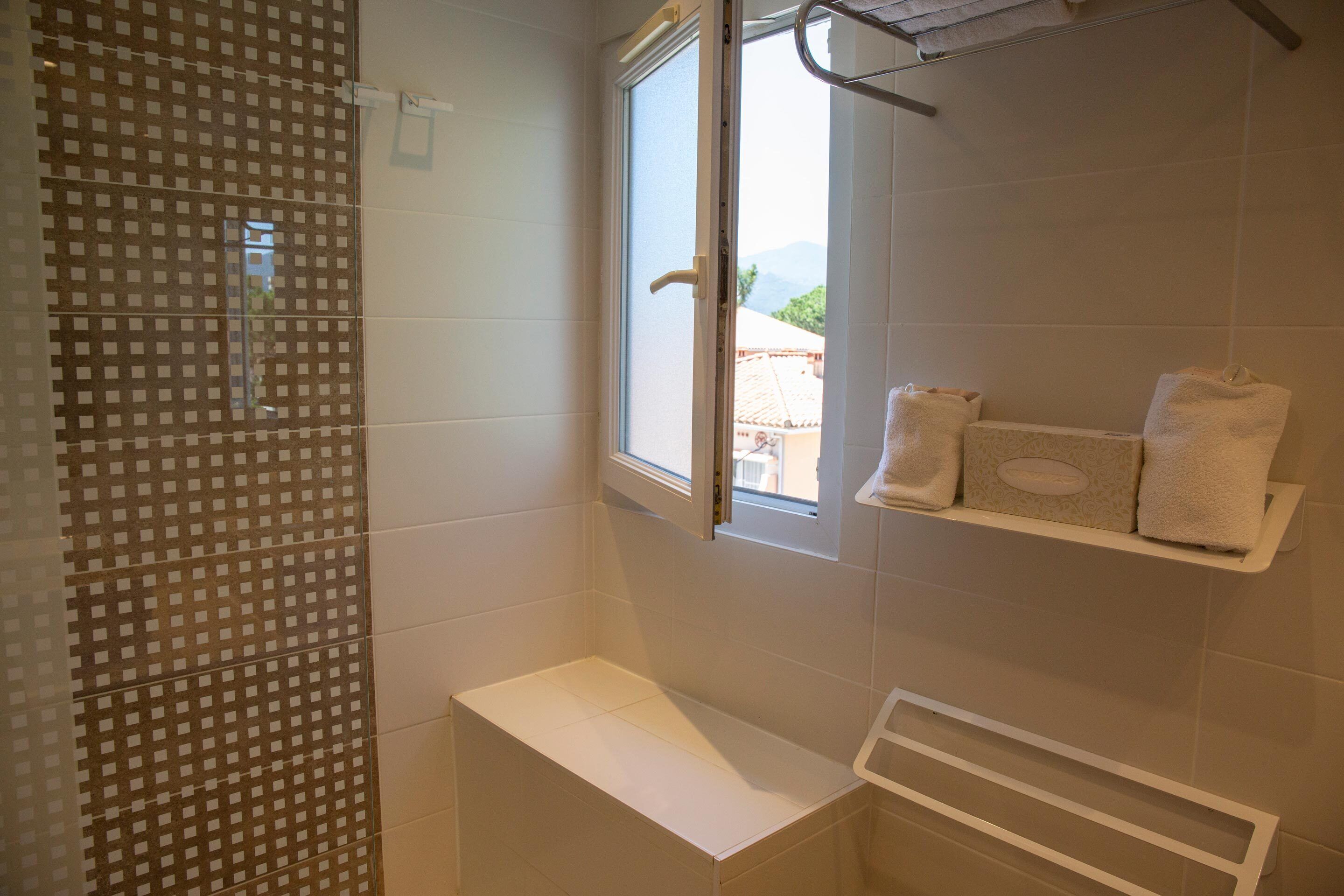 A bathroom with a shower, a window, and a shelf with towels.