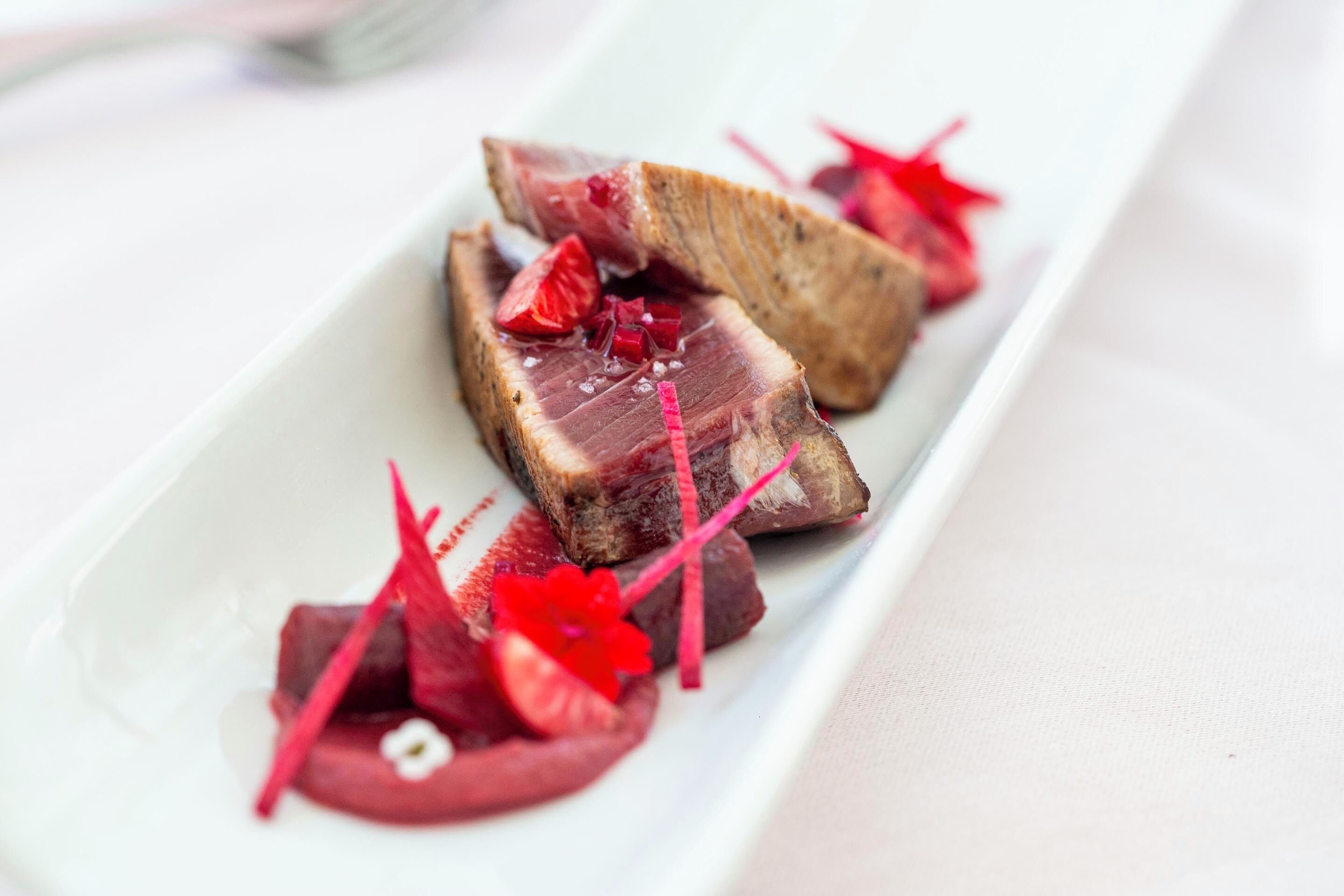 Un plato rectangular blanco con rebanadas de carne y guarniciones rojas.