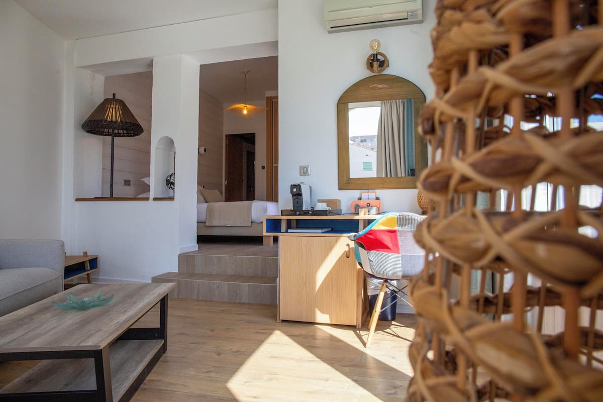 Una sala de estar moderna con un sofá, una mesa de centro y una silla de mimbre. Hay una zona de cocina con una encimera y un fregadero.