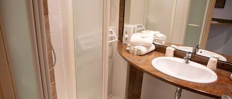 A bathroom with a granite countertop, a white sink, a mirror, and a glass shower enclosure.