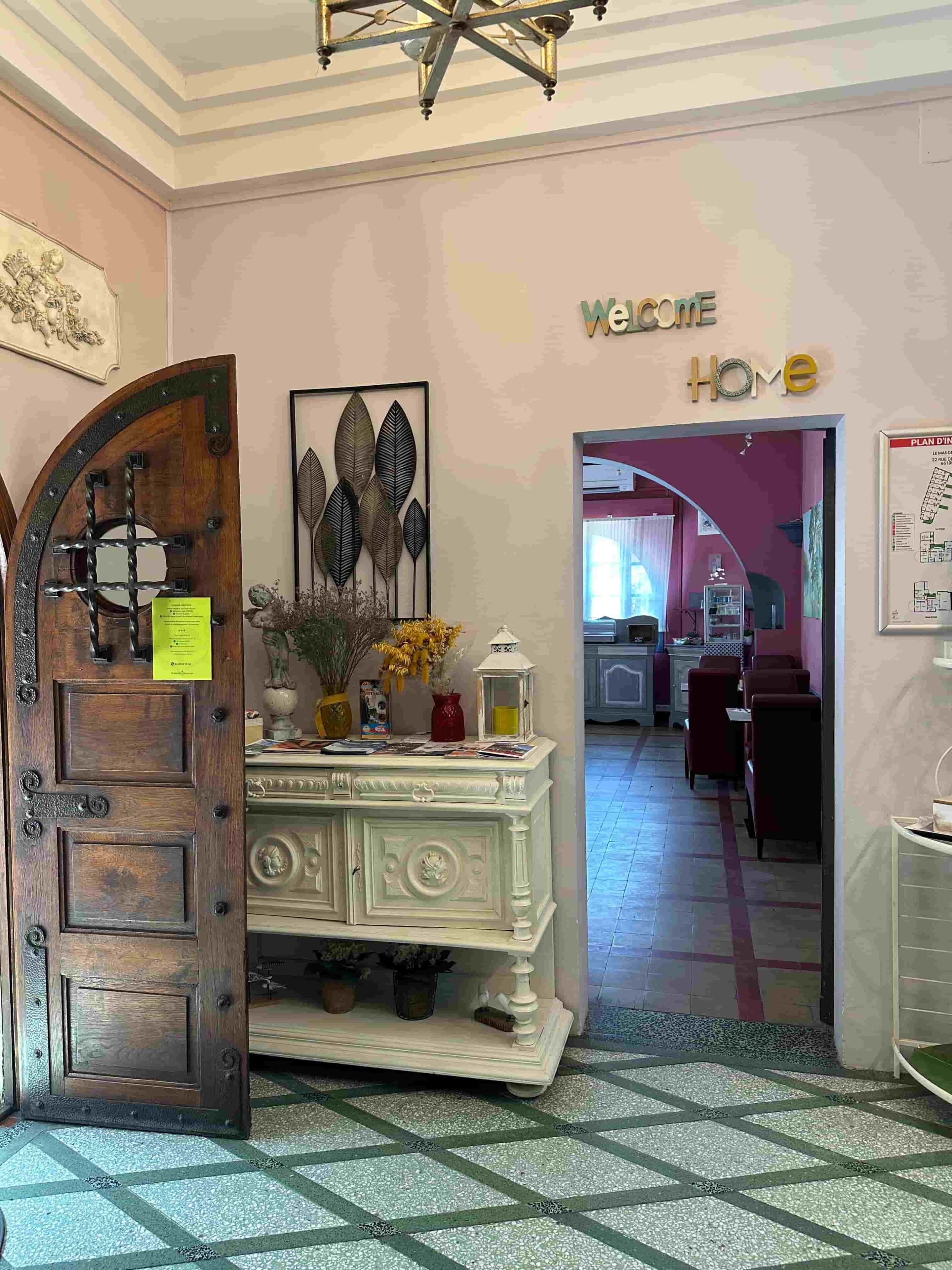 Un espace d’accueil avec une porte en bois, une console blanche agrémentée d’objets décoratifs et un panneau indiquant : « Bienvenue chez vous ».