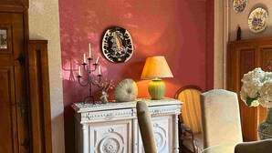 A room with a white ornate cabinet, a candelabra, a lamp, and a chair with a vase of flowers. - Hôtel Le Mas des Citronniers (Collioure)