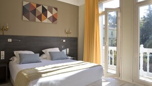 A bedroom with a large bed, two bedside tables, a wall-mounted artwork, and a sliding glass door leading to an outdoor area. - Hôtel Le Mas des Citronniers (Collioure)