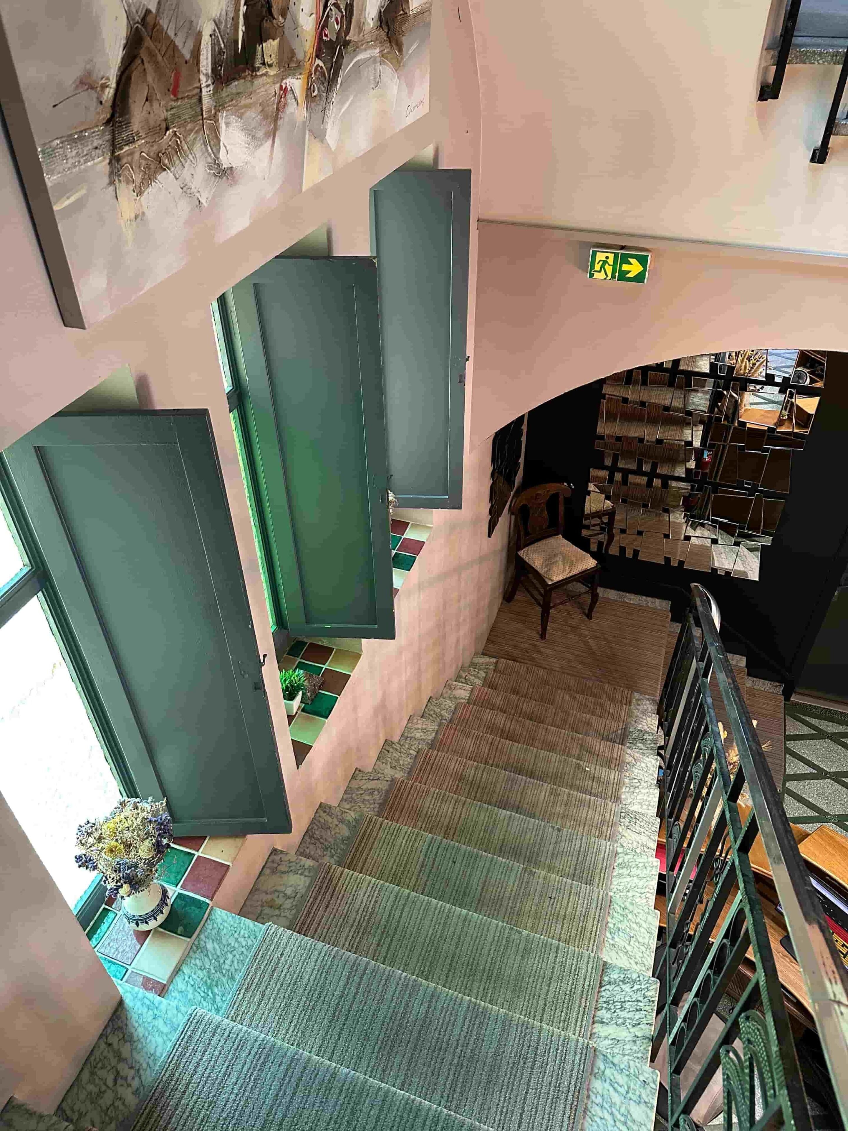 A staircase with a patterned carpet leading to a lower level, a green door, and a wall with a grid of square panels.