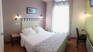 Un dormitorio con cama, mesitas de noche, un escritorio, una silla, una ventana con cortinas y un televisor de pared.