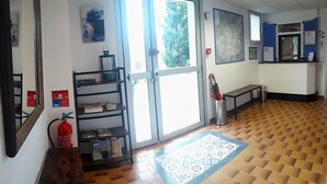 Un vestíbulo con piso de madera, un mostrador de recepción, un extintor, un bote de basura metálico y un mapa en la pared.