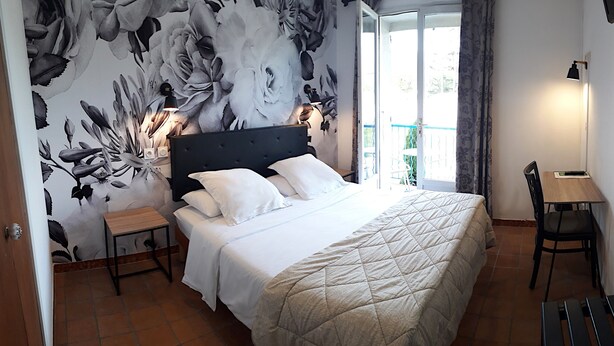 Un dormitorio con cama, mesita de noche, silla y vistas al exterior.