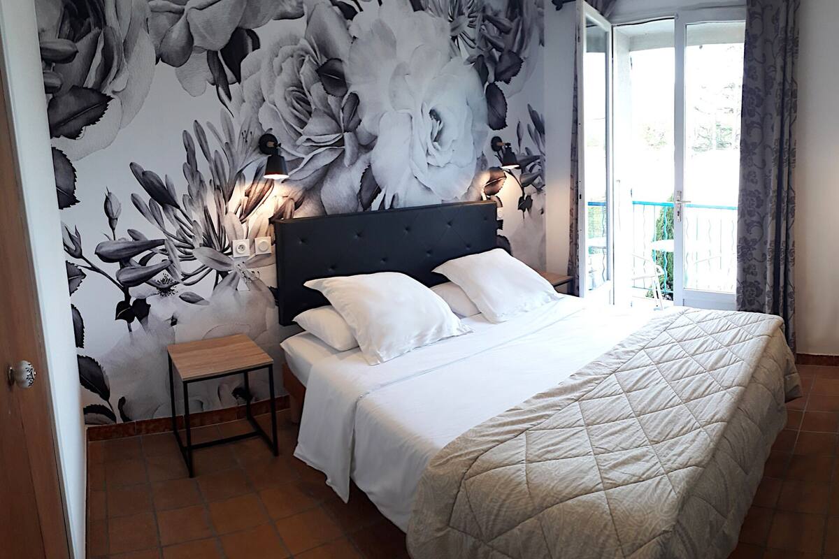 Un dormitorio con cama, mesita de noche, silla y vistas al exterior.