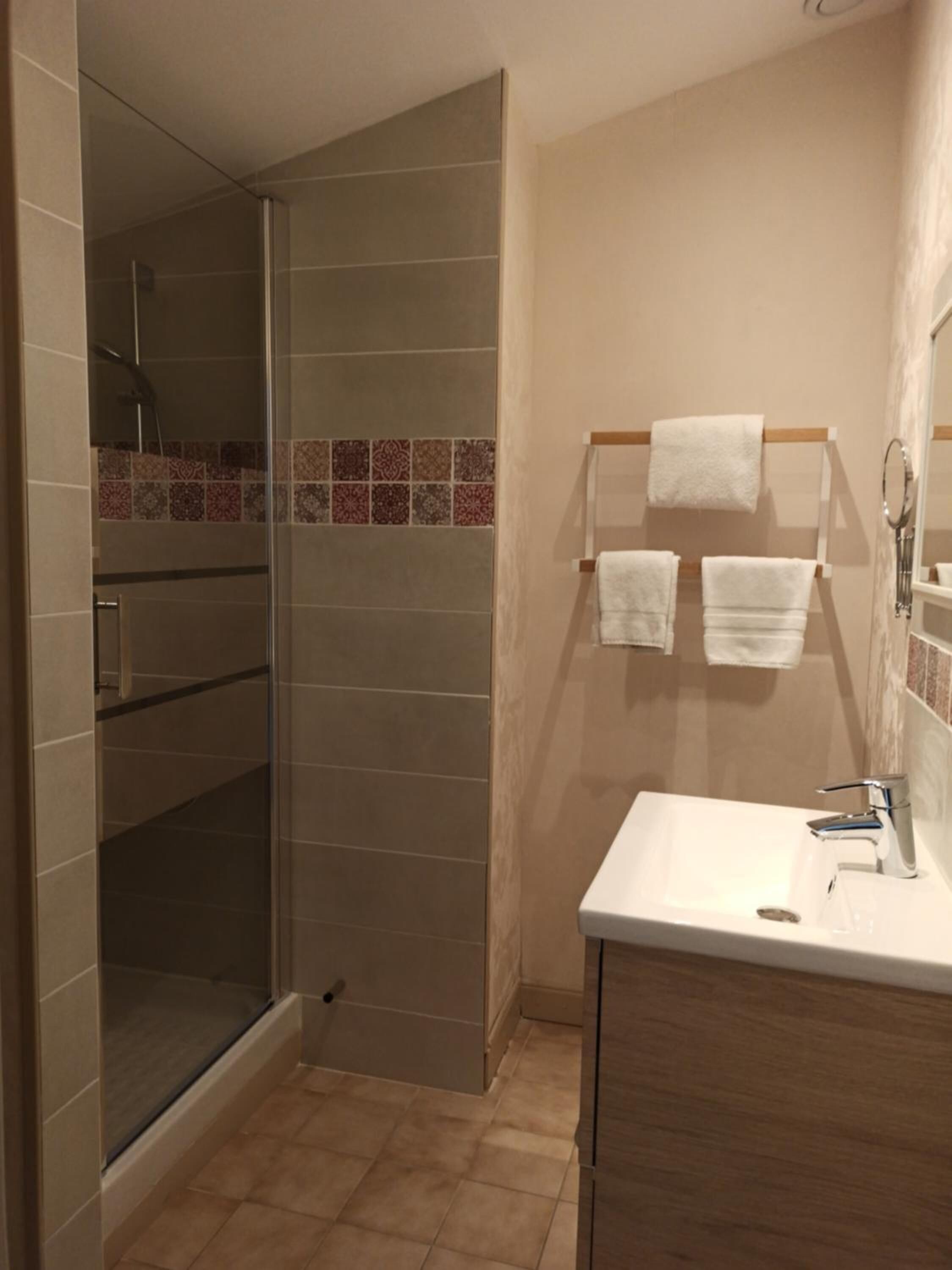 Un baño con cabina de ducha de vidrio, un lavamanos blanco y un perchero con tres toallas.
