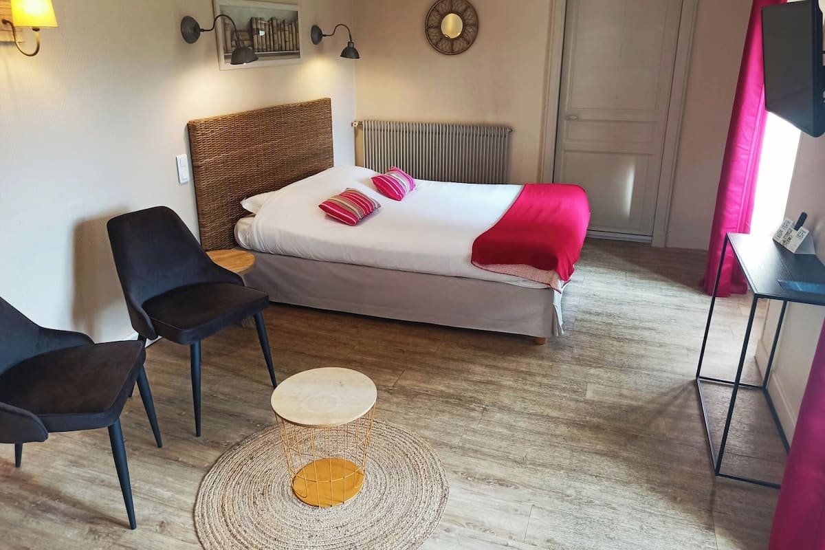 A hotel room with a bed, two chairs, a small table, a radiator, and a door.