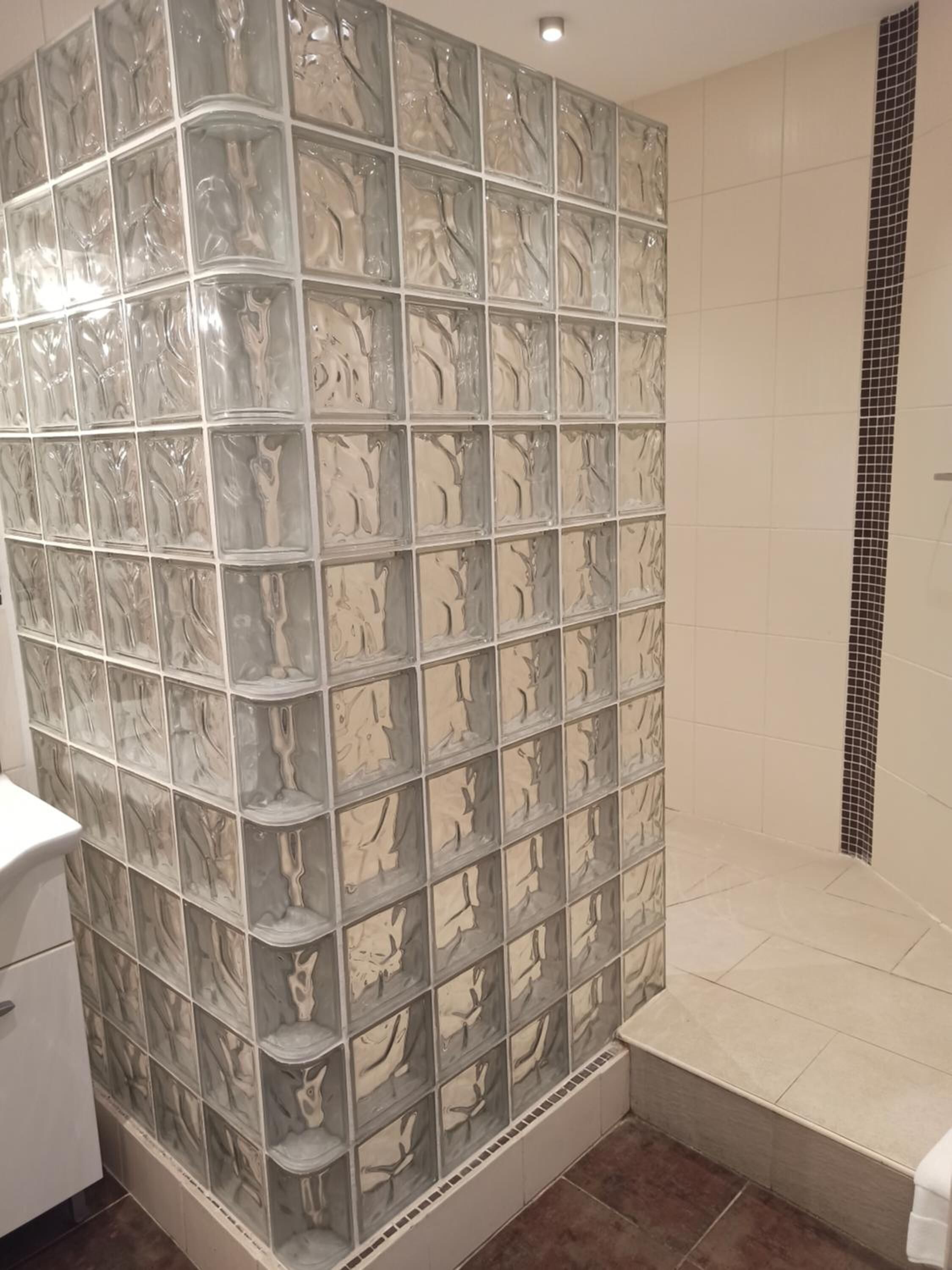 Een badkamer met een glazen scheidingswand, een wit wastafelmeubel en een betegelde douchehoek.