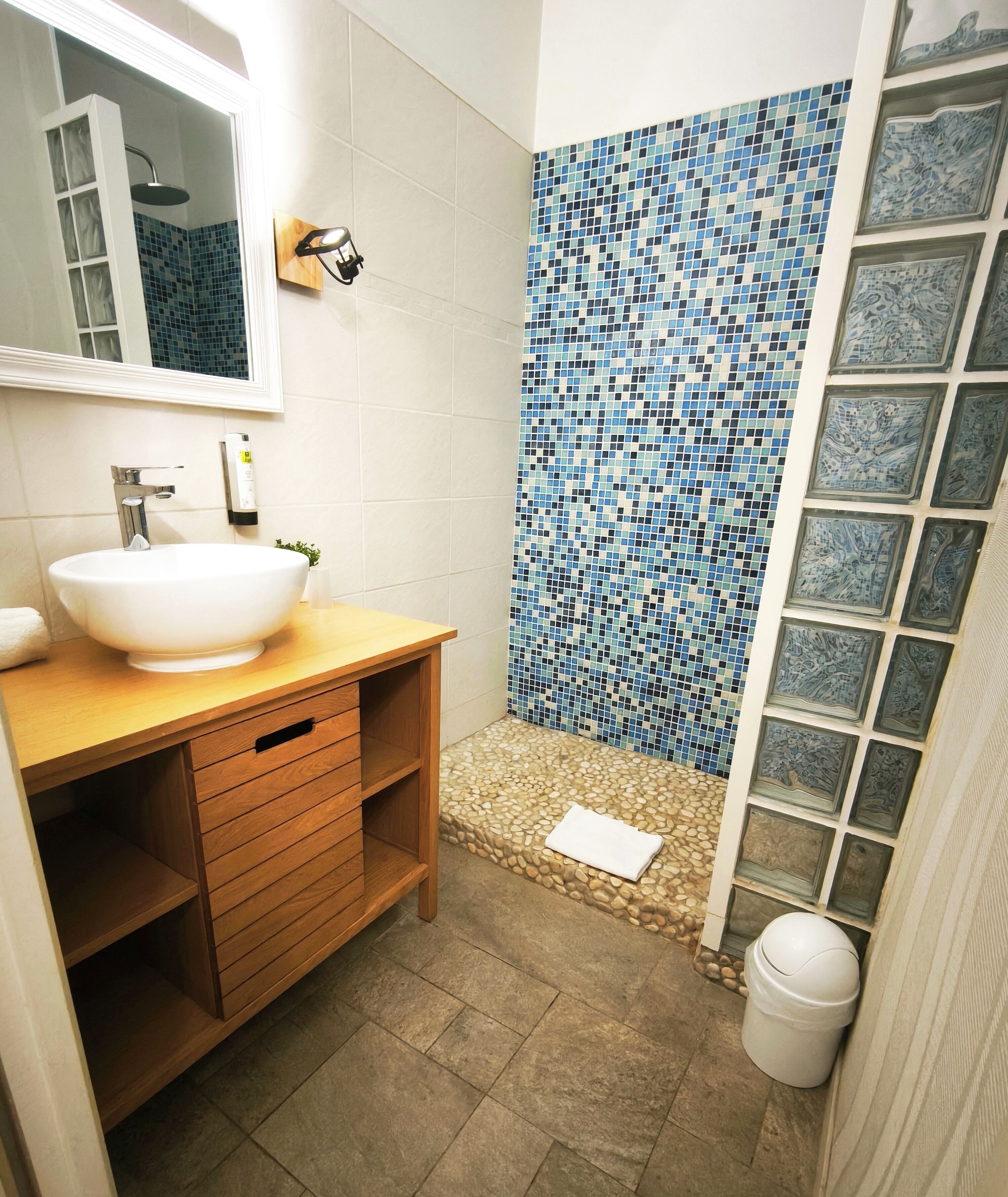 A bathroom with a white sink, wooden vanity, tiled shower, and a mirror.