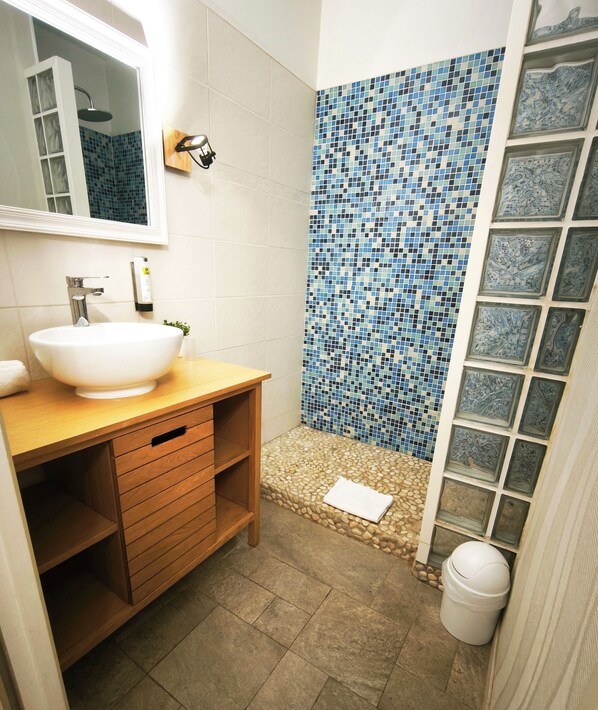 A bathroom with a white sink, wooden vanity, tiled shower, and a mirror.