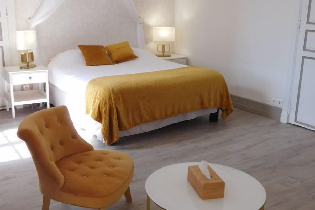 Una habitación de hotel con una cama, mesitas de noche, una silla y una mesa redonda.