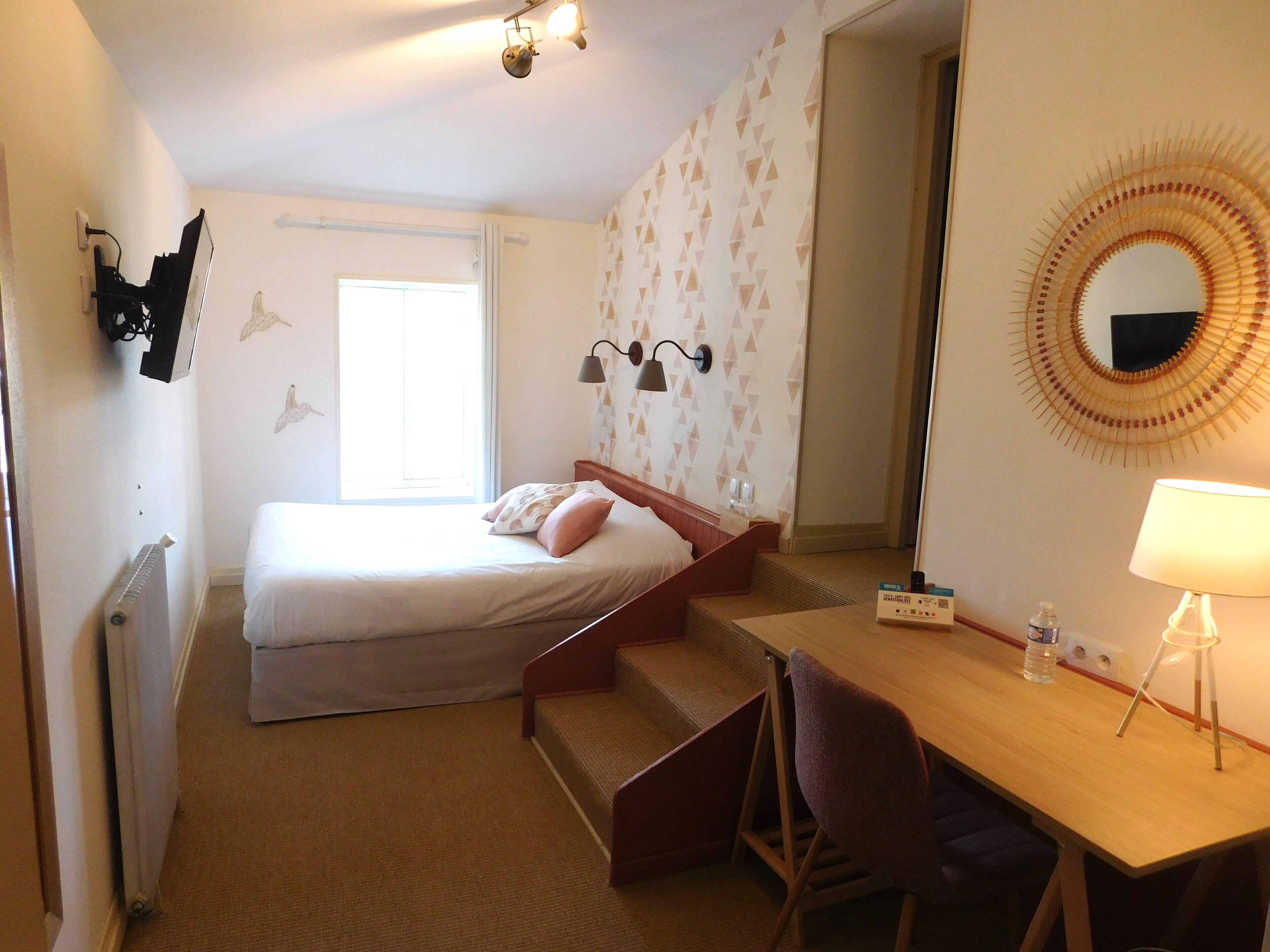 Een hotelkamer met een bed, een bureau, een stoel, een spiegel en een radiator.